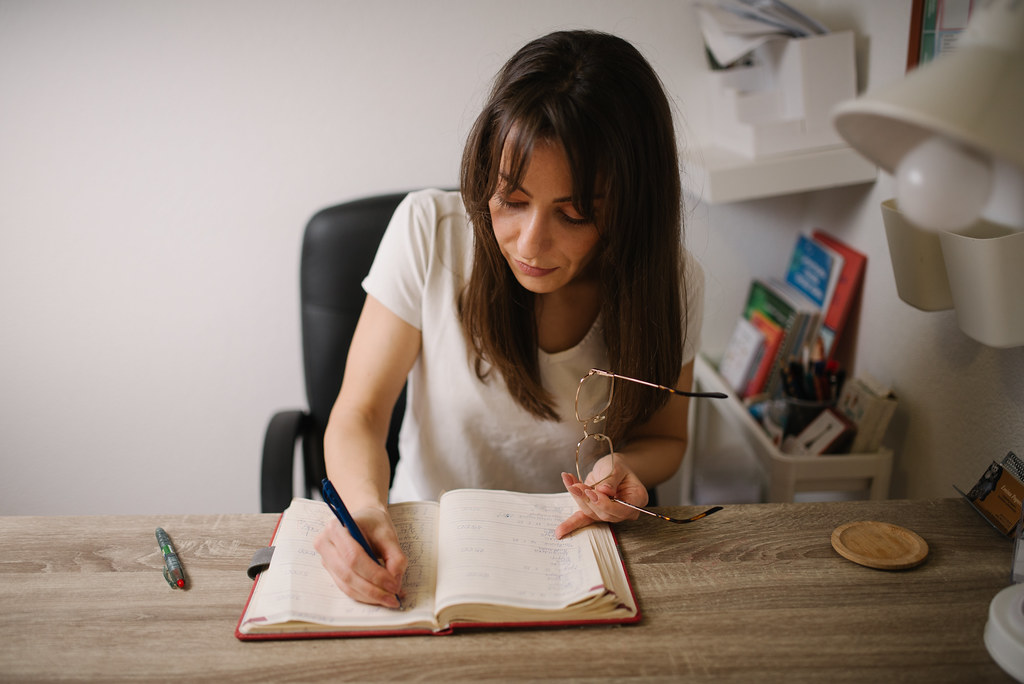 A young woman sitting at a wooden desk, writing in a notebook.