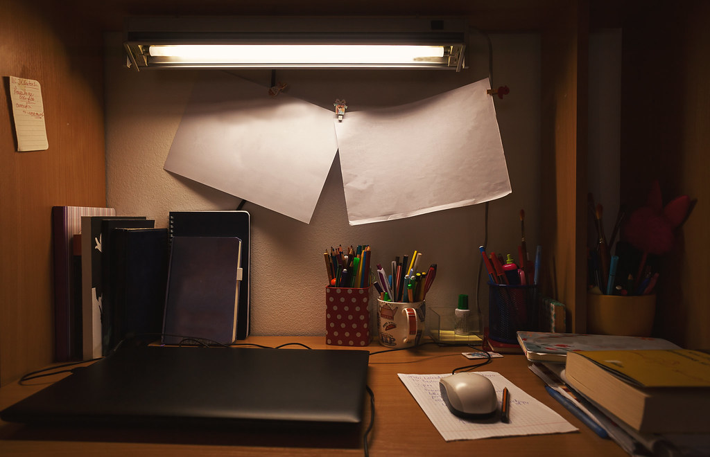 A small home working table at dusk with a lamp and a notebook.